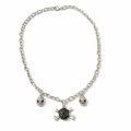 A silver-toned chain necklace featuring three skull and crossbones charms, with the center charm in black and the side charms in silver