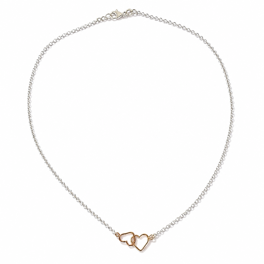 A delicate silver chain necklace with two interlocking open heart charms in a warm rose gold tone